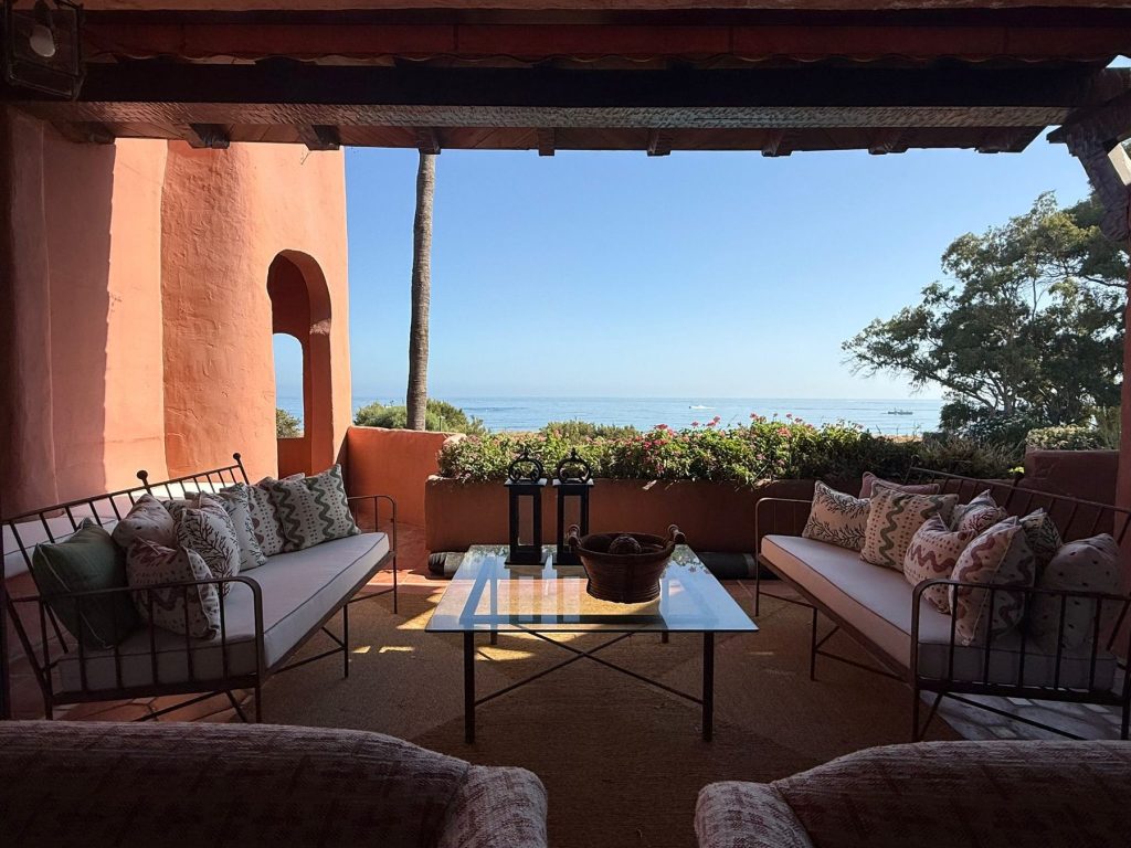 Terraza con muros encalados en tono albero, sofás de forja con cojines estampados y vistas al mar — proyecto de interiorismo en Marbella