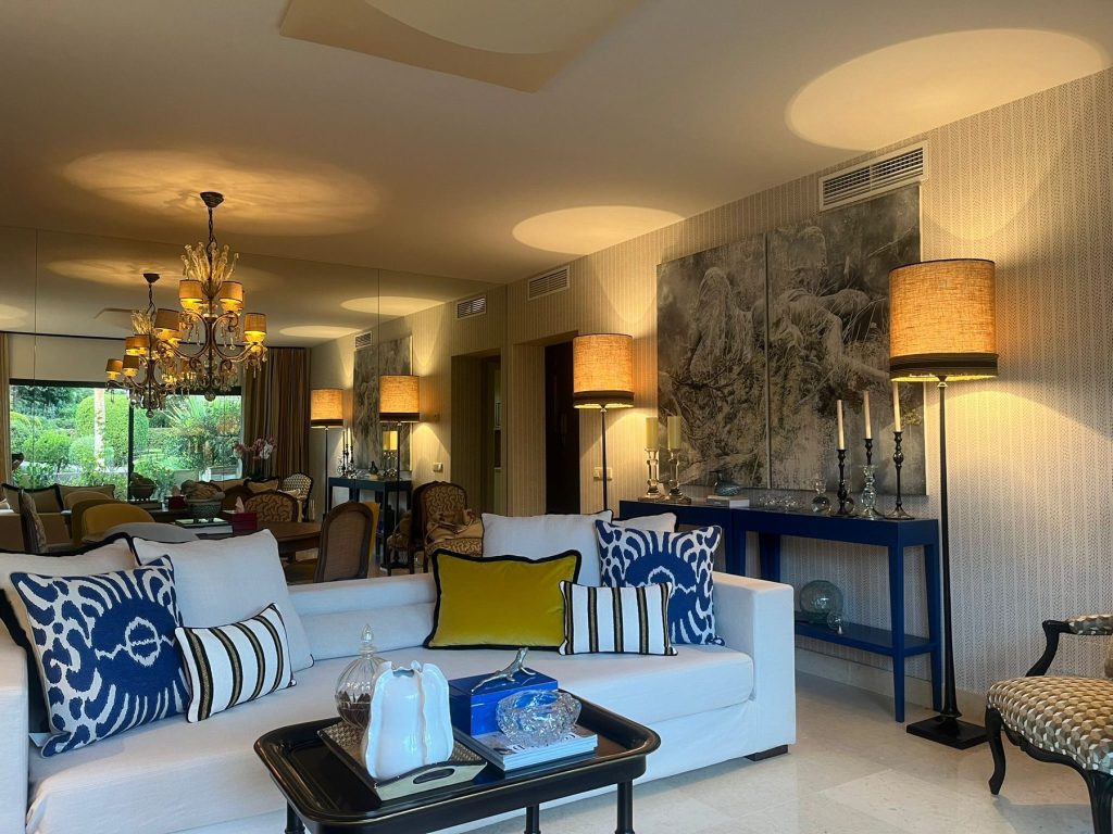 Salón con papel pintado de paisaje chinoiserie, sofás blancos con cojines de rayas azules y consola lacada en azul cobalto