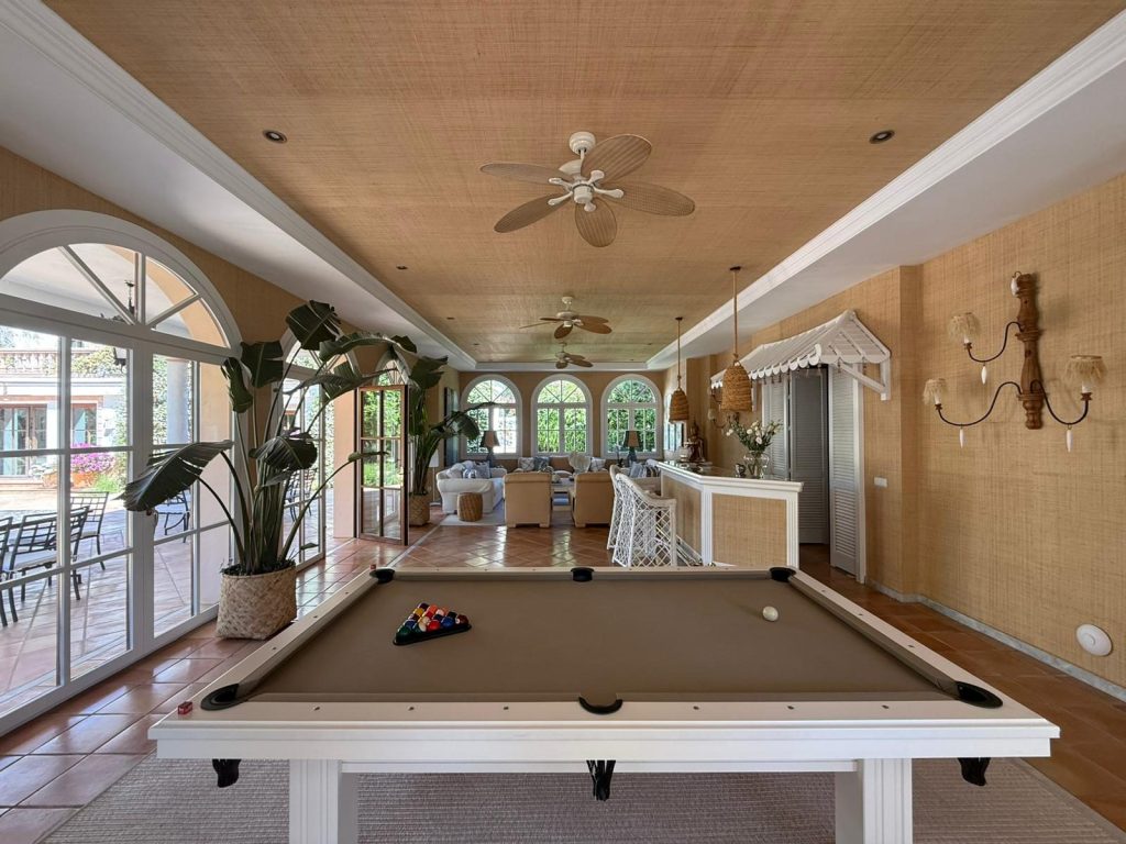 Sala de juegos con mesa de billar bajo techo de madera, ventanales arqueados y barra al fondo — villa en Marbella
